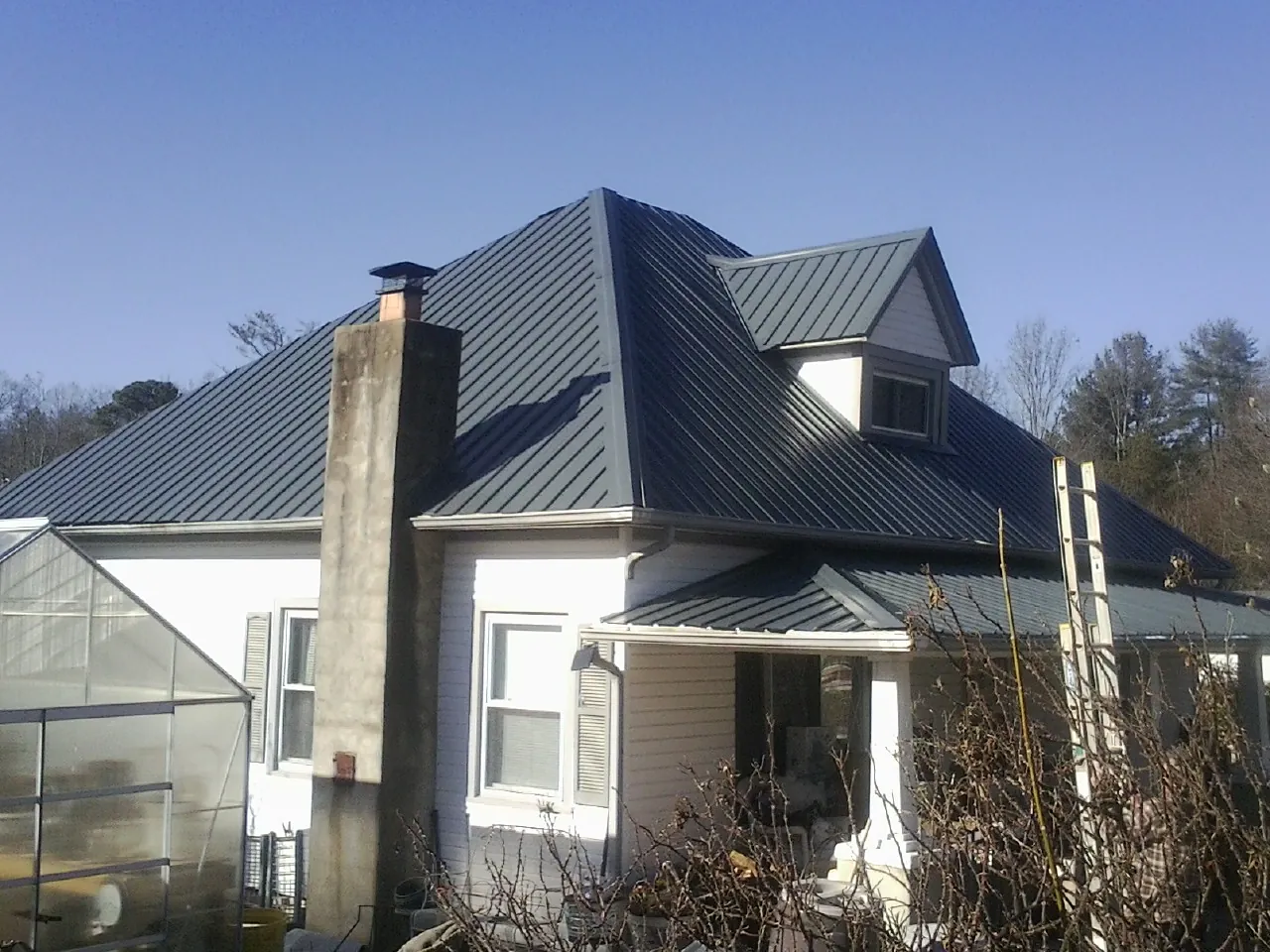 Dark blue standing seam metal roof on a white farmhouse with dormer — Slate & Tile Roof Repair by Roofing Brothers in Boscobel