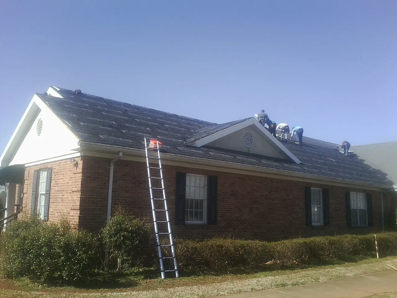Crew tearing shingles off a brick ranch roof with a ladder set — Emergency Roof Repair work by our crew in Boscobel