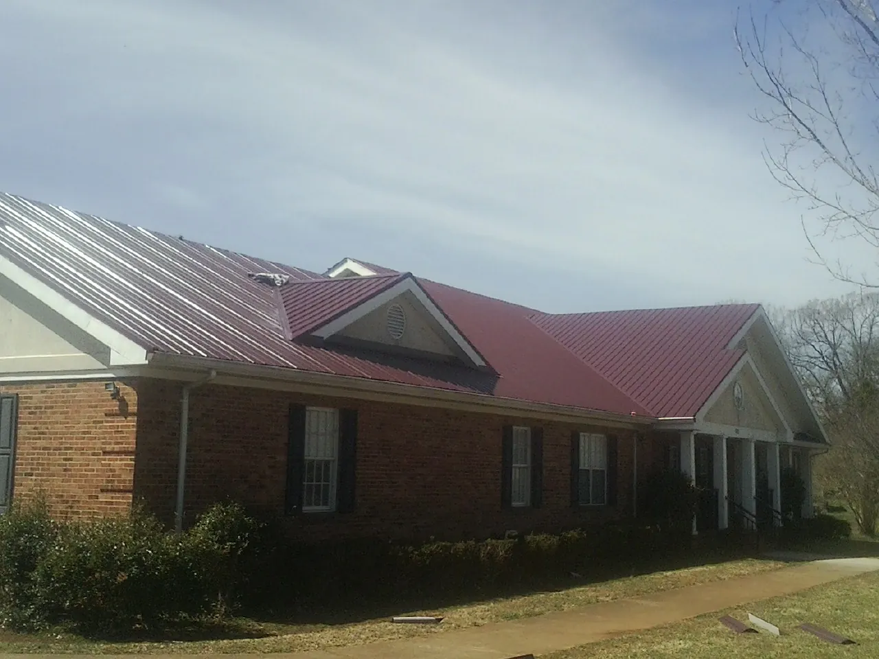 Red metal roof with gabled entries on a long brick building, from a Hail Damage Roof Repair job in Boscobel