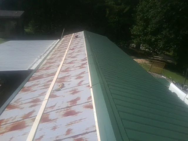 Old rusted panels beside newly installed green metal roofing — Wind Damage Roof Repair by Roofing Brothers in Boscobel