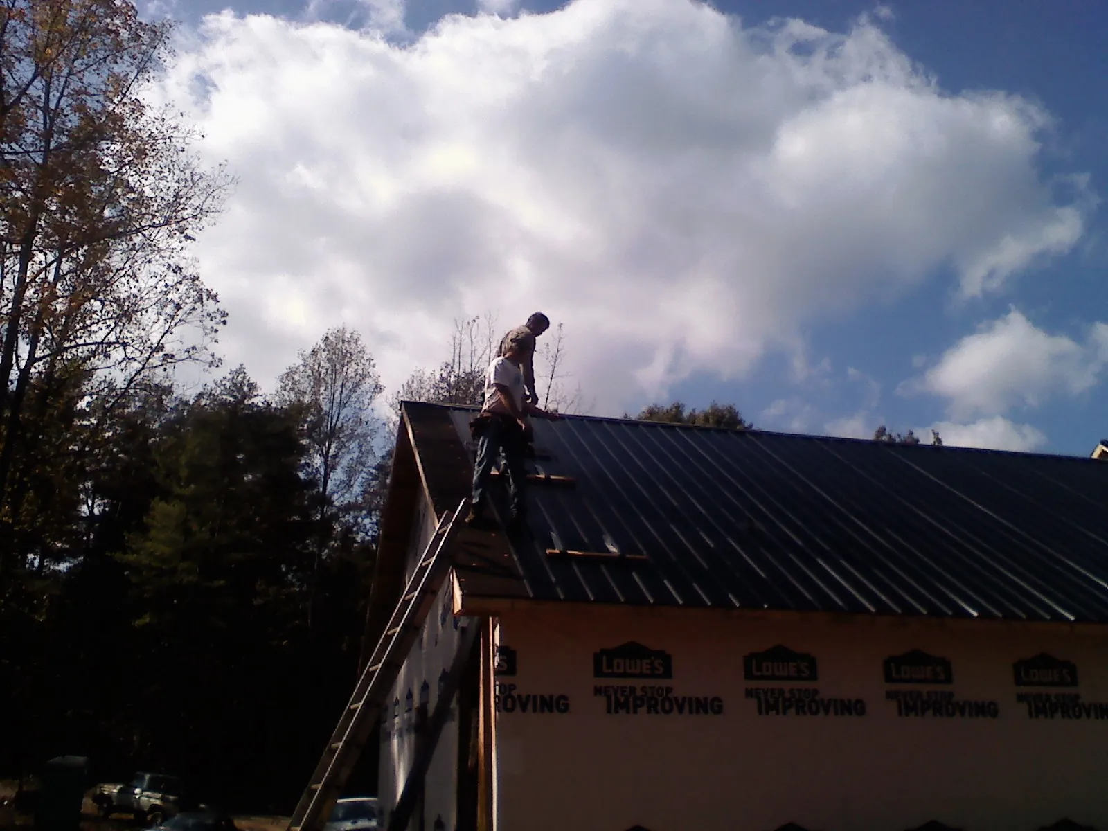 Roofer fastening dark metal panels high against a cloudy sky, from a Roof Inspection job in Boscobel