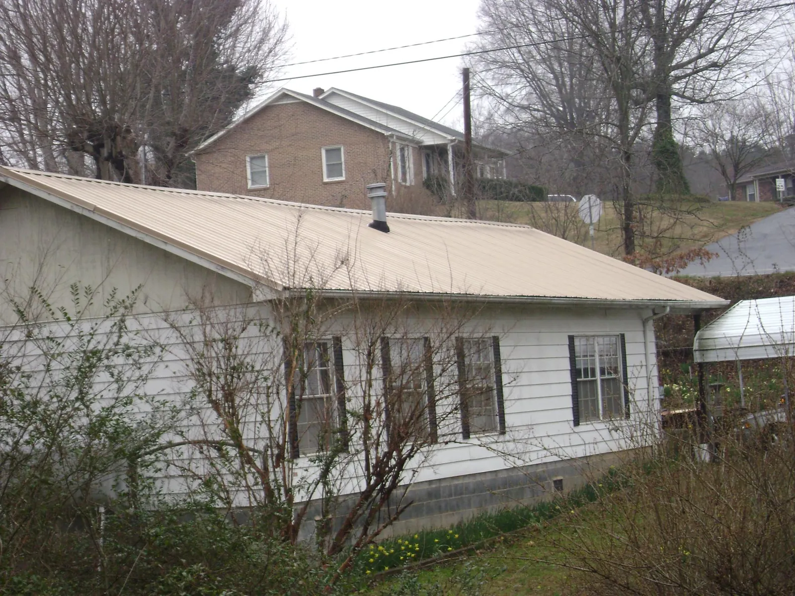 Tan metal roof on a white sided house set into a hillside — Commercial Roofing by Roofing Brothers in Boscobel